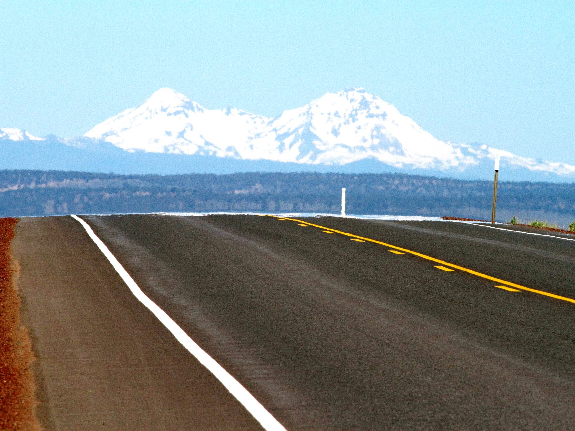 Close-up view of roadway on U.S. Route 20 with snow-capped mountains in the distance