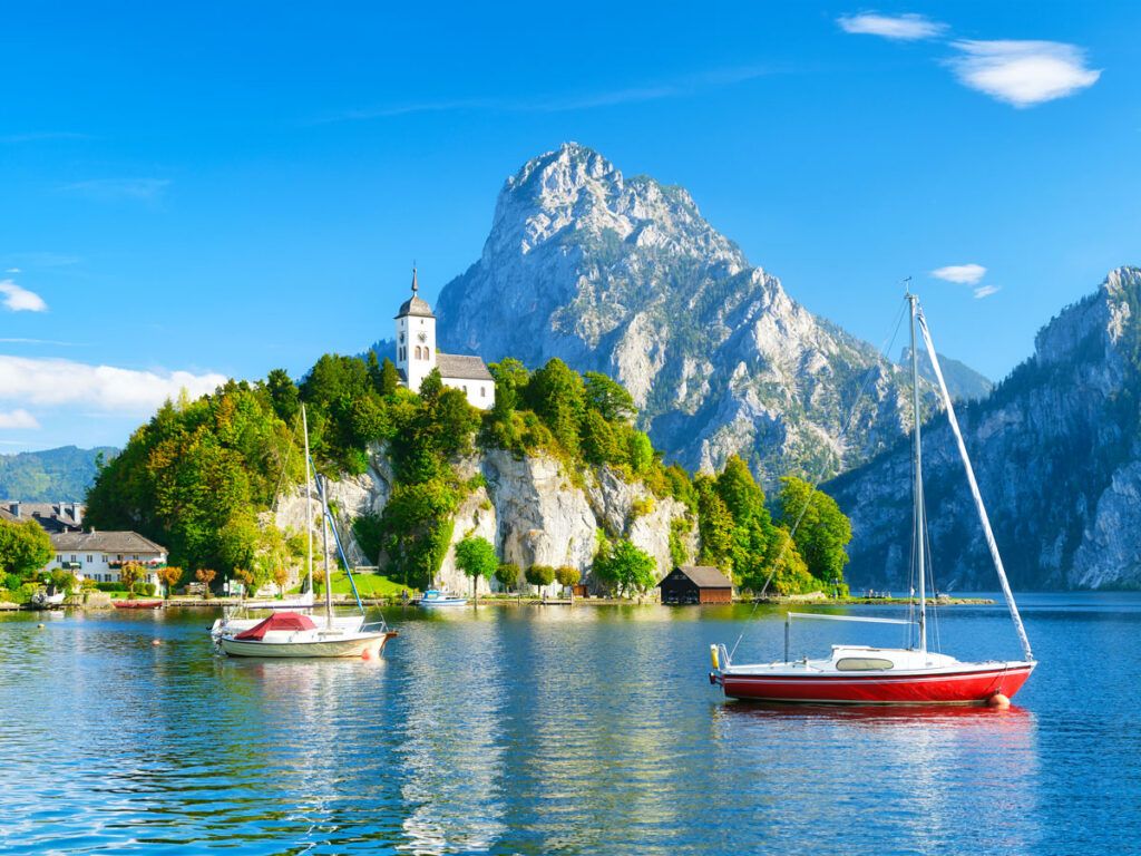 Sailboats moored in Swiss lake with church and mountains in background