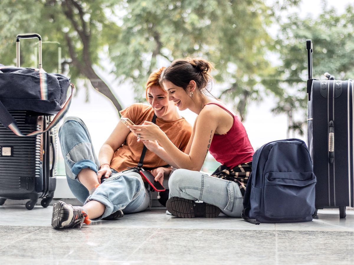 Pair of travelers sitting on floor looking at phone next to their luggage