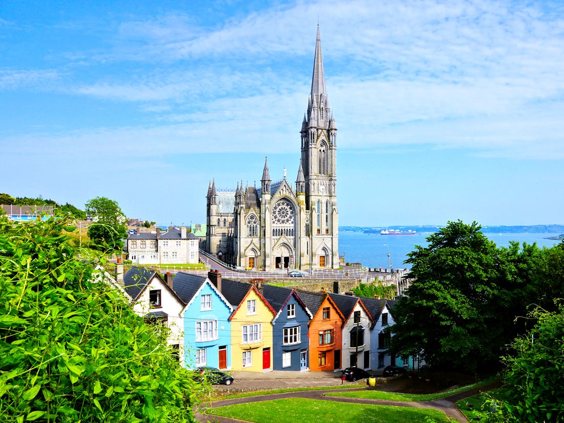 Colorful row houses on hill with church towering in background in Cobh, Ireland 