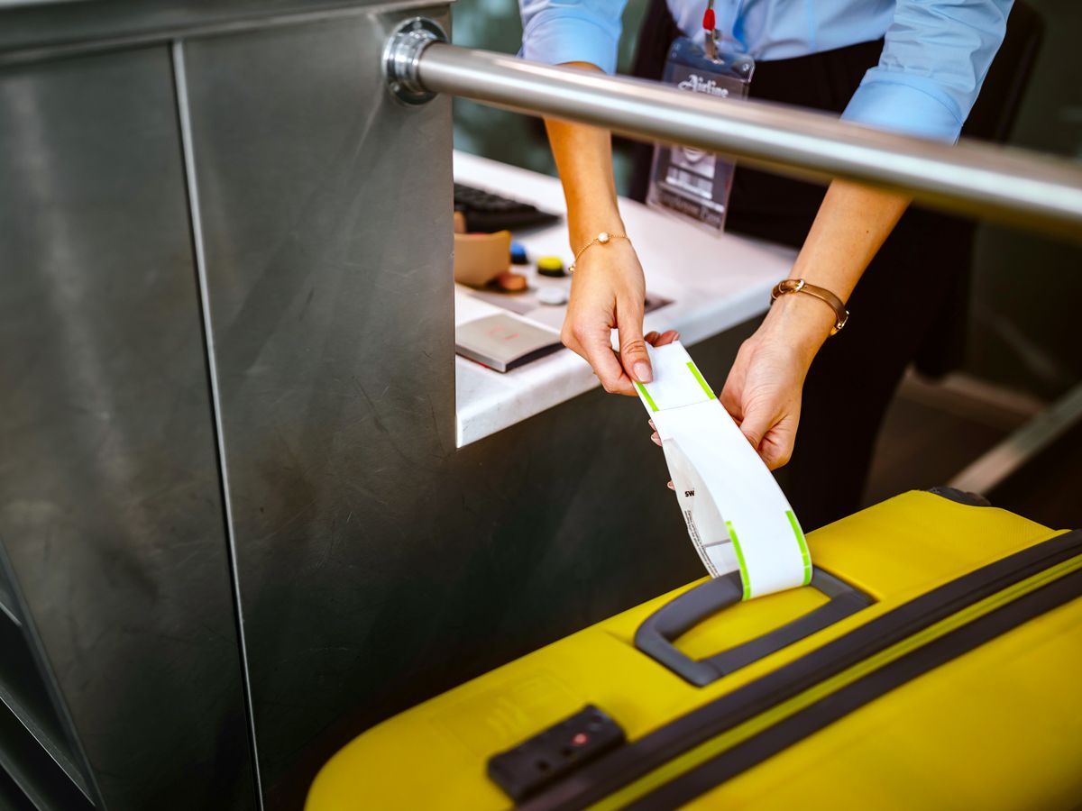 Airport employee placing bag tag on luggage at check-in counter