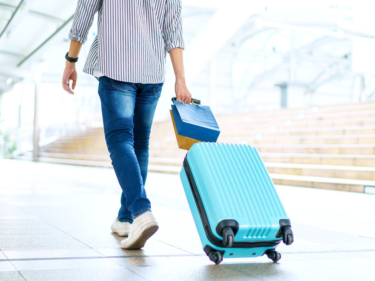 Traveler rolling suitcase and shopping bags through airport