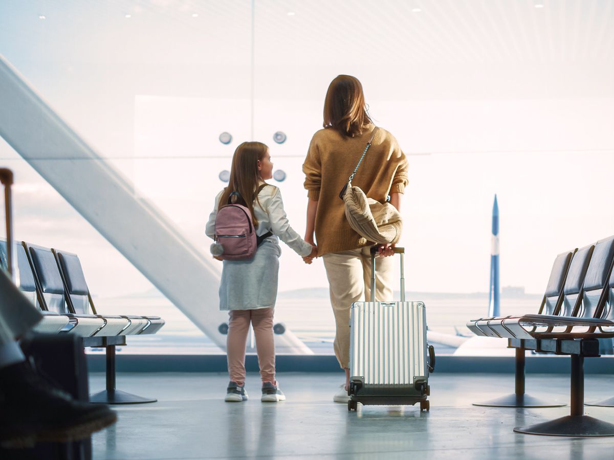 Mother and daughter holding hands looking out airport window