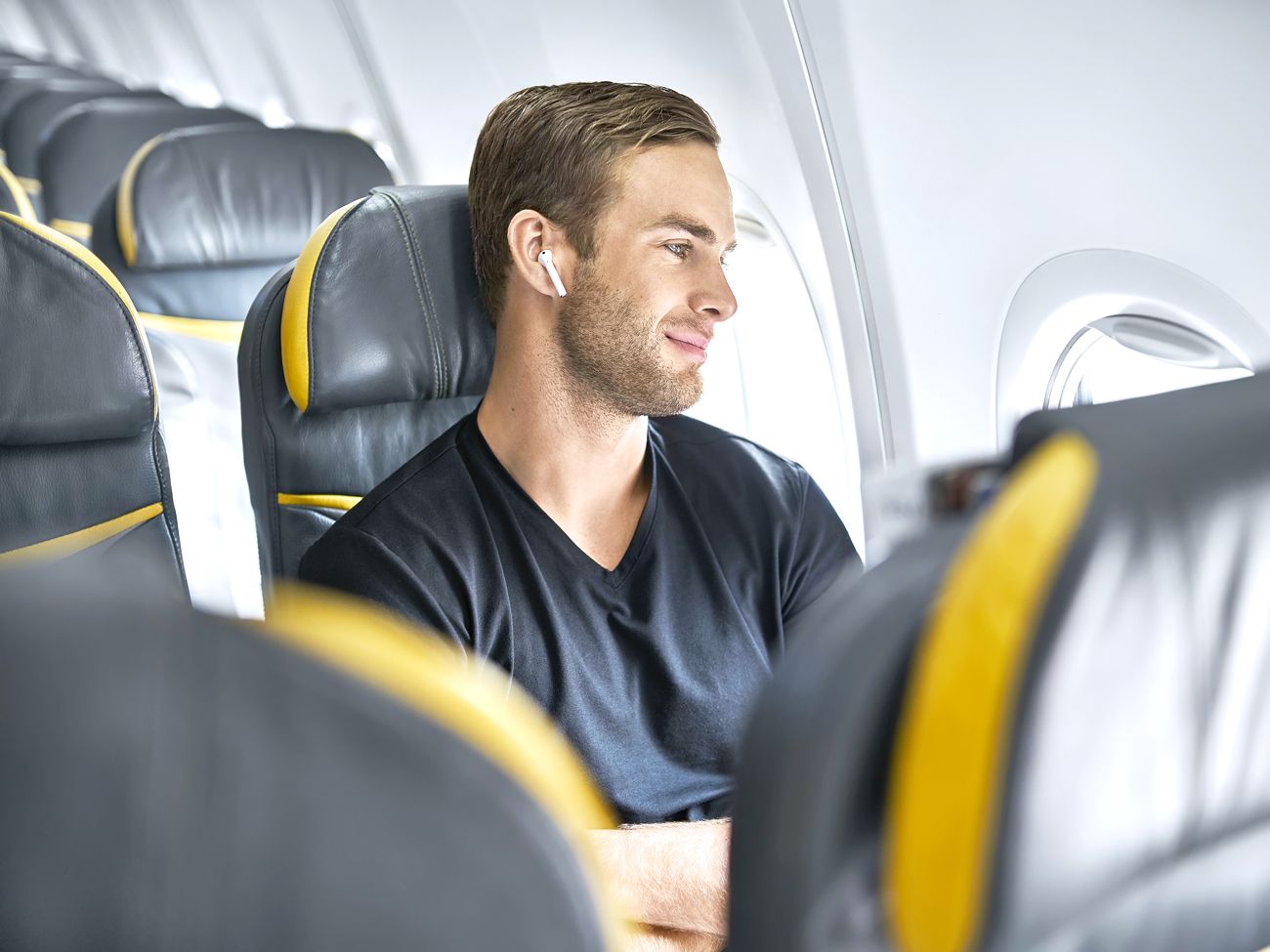 Airline passenger in seat wearing Bluetooth headphones