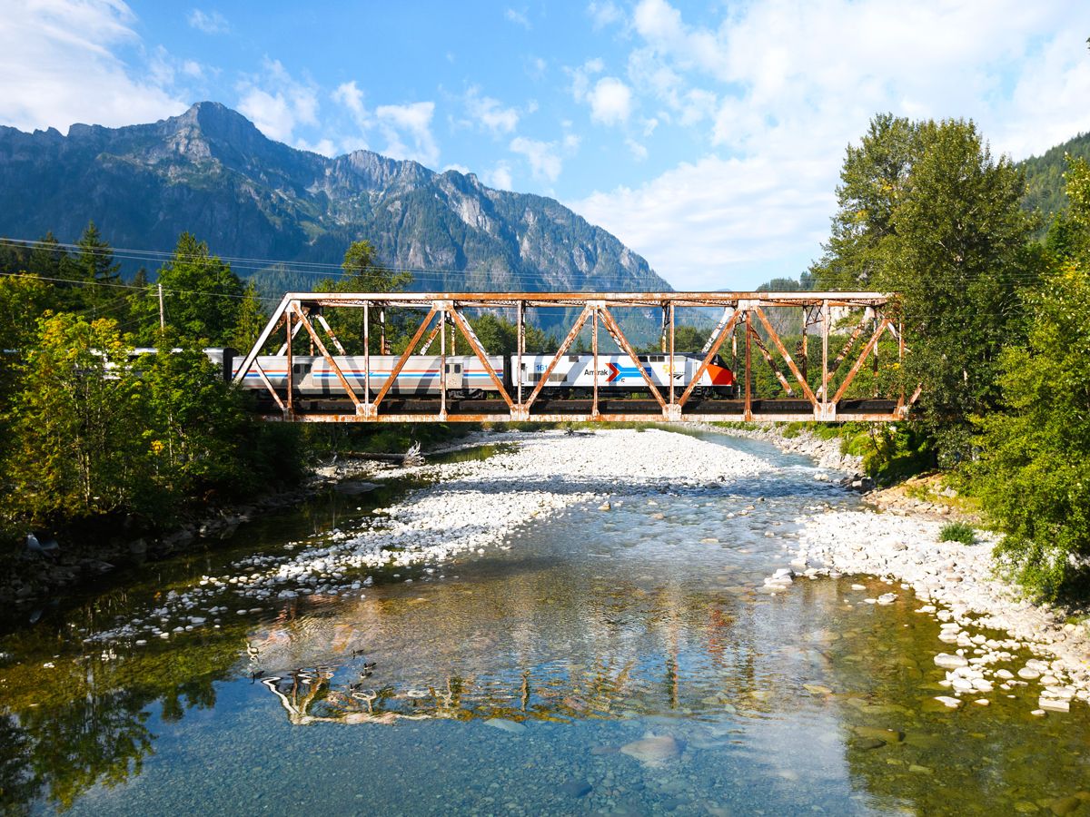Amtrak train crossing bridge with mountains in background