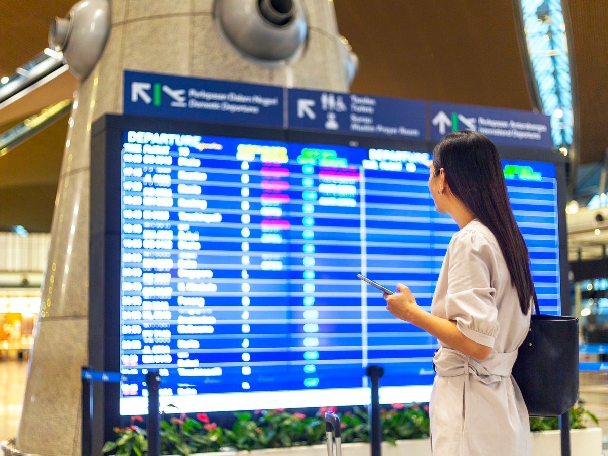 Airline passenger looking at departures and arrival board in airport terminal