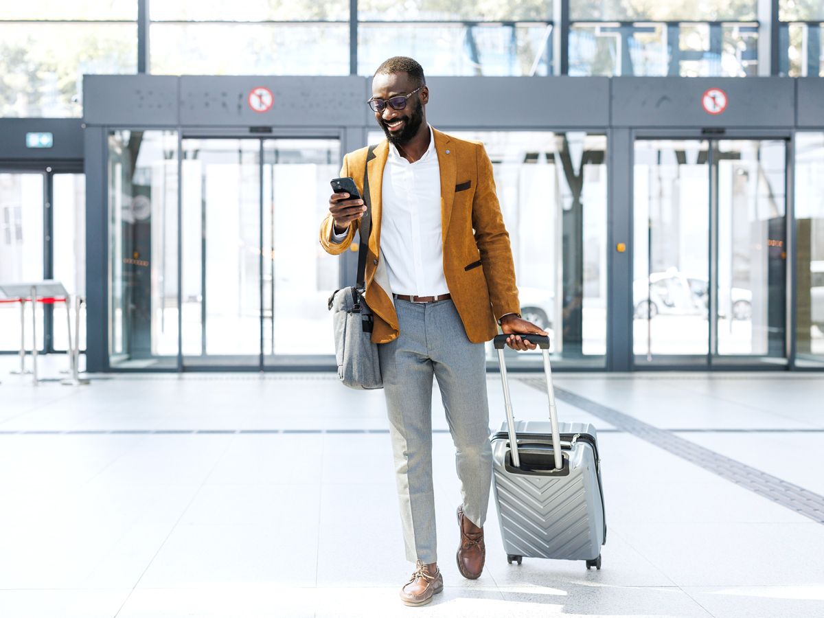 Traveler walking through airport with suitcase while using phone
