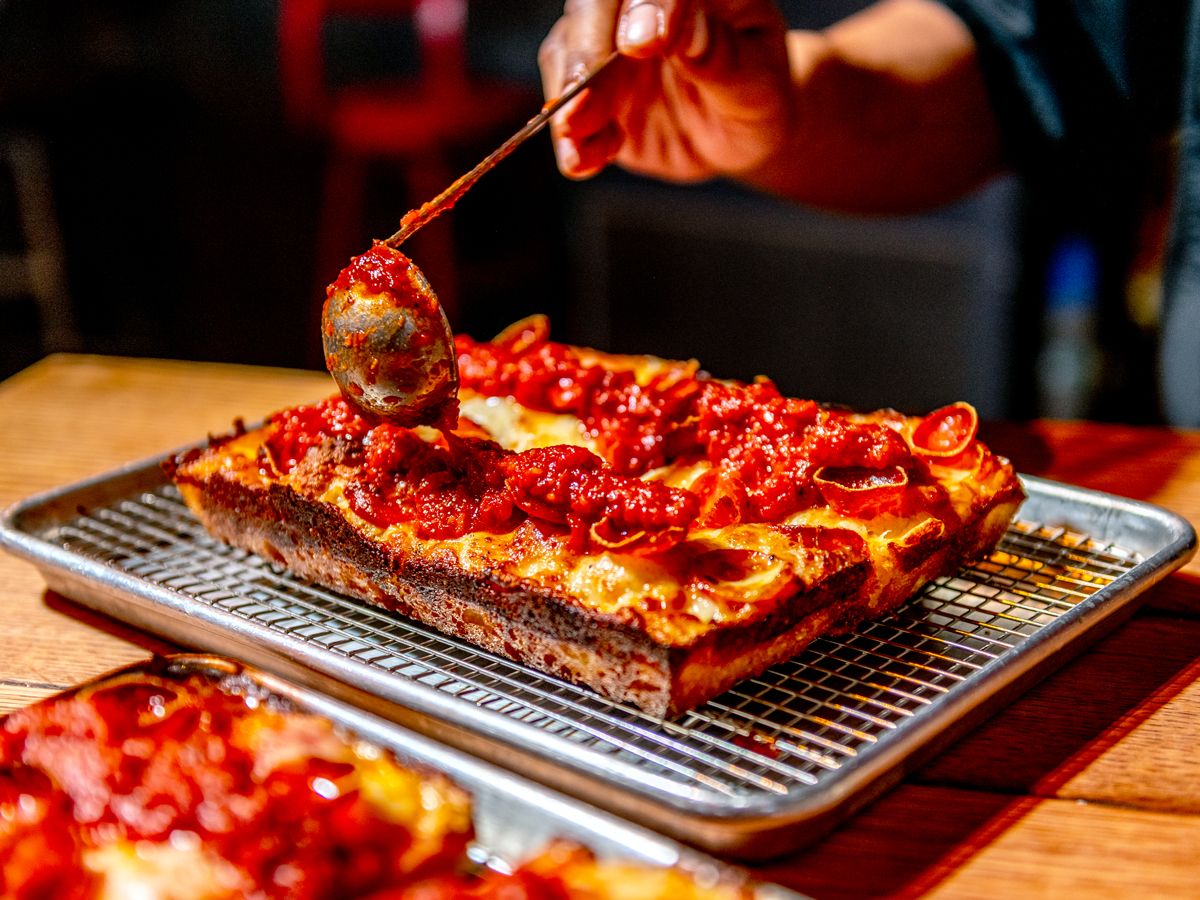 Chef placing sauce on Detroit-style pizza in pan