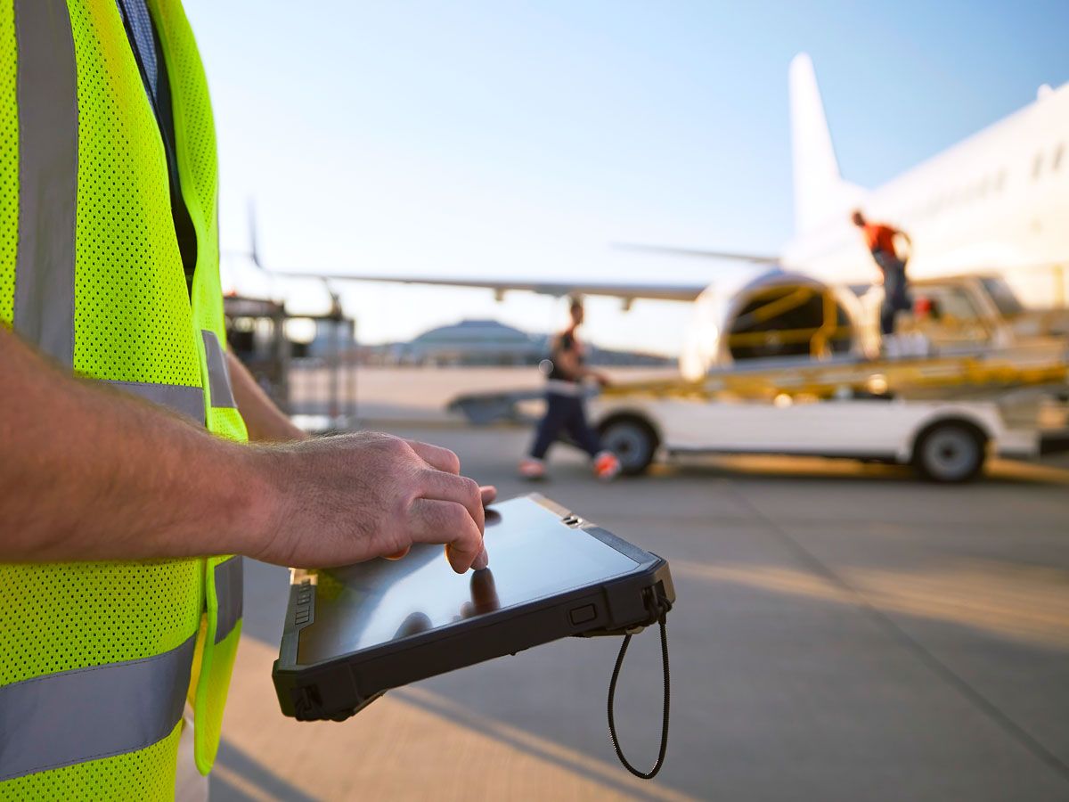 Ramp agent using tablet next to aircraft parked at gate