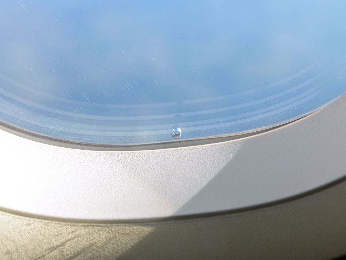 Close-up view of small round hole at bottom of aircraft window