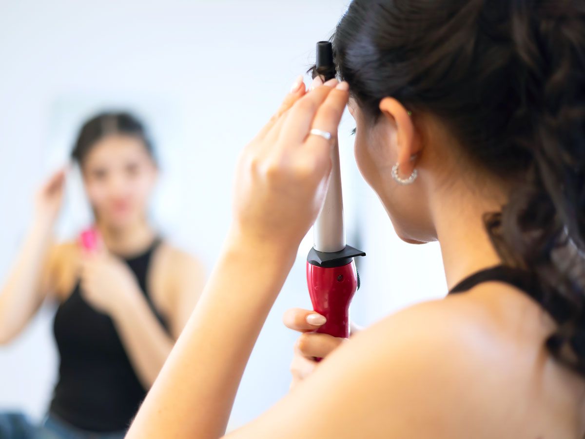 Woman using curling iron looking at mirror