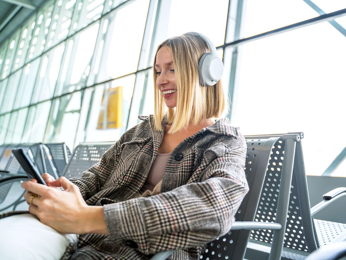 Traveler sitting in airport terminal with headphones and cellphone