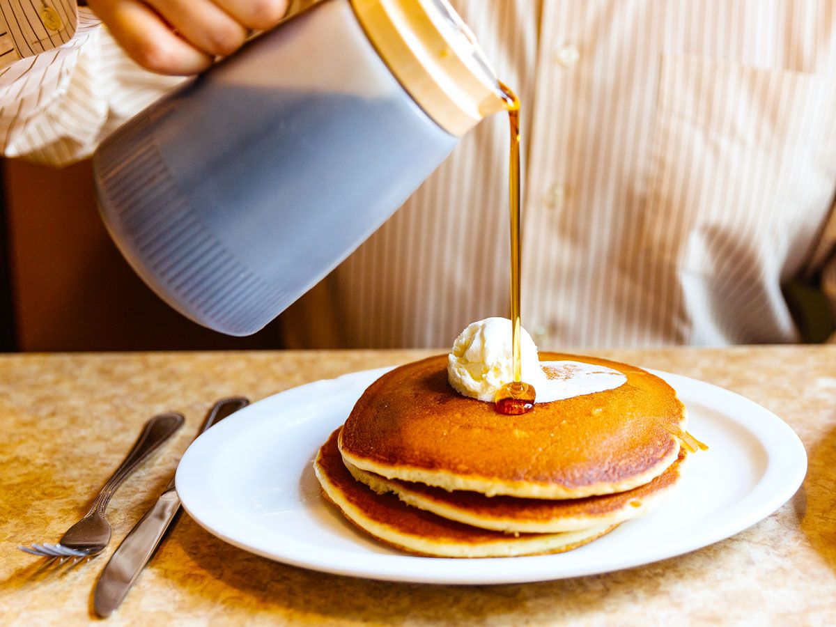 Person pouring maple syrup on stack of pancakes