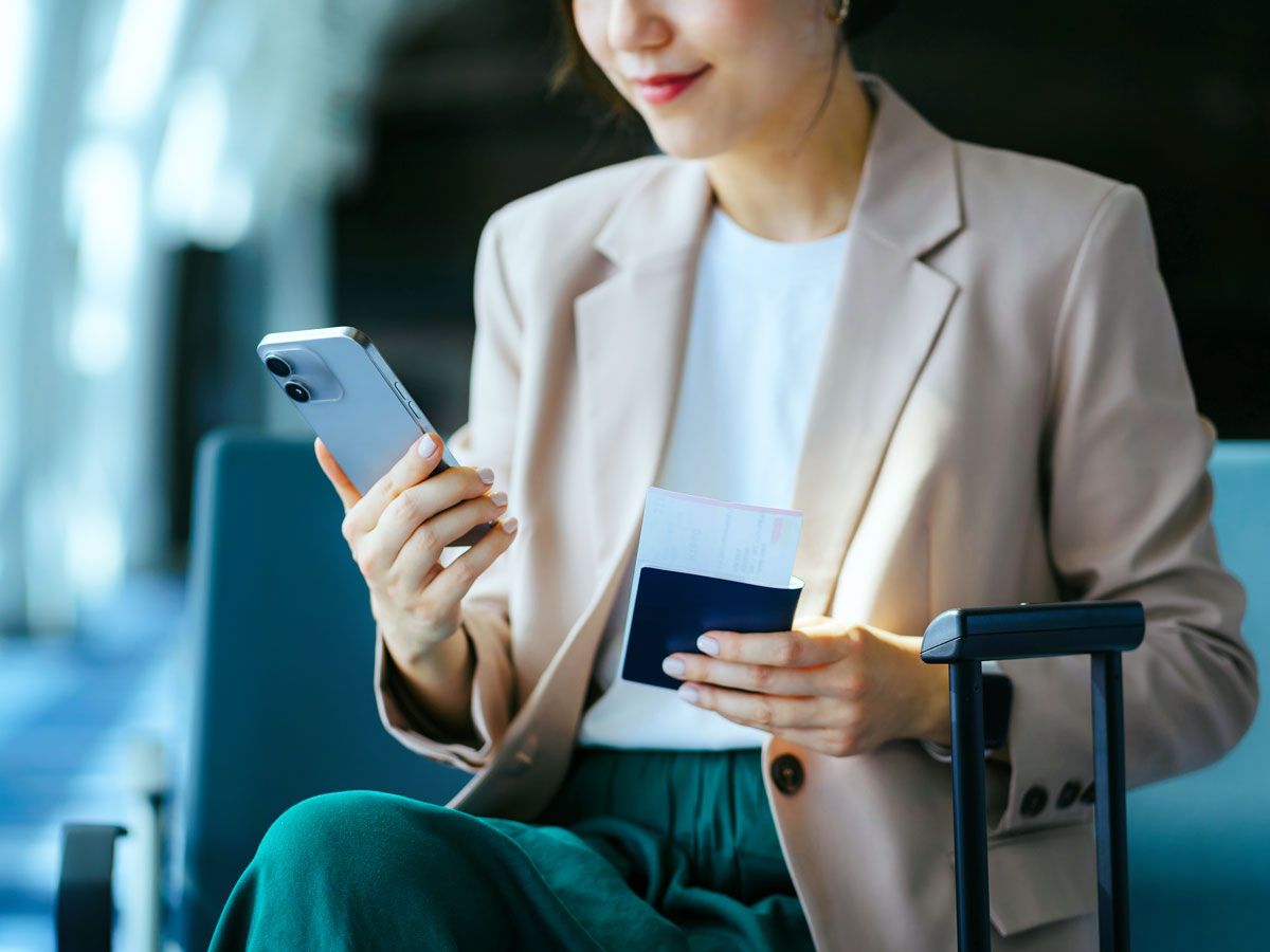 Traveler looking at phone while holding passport and boarding pass