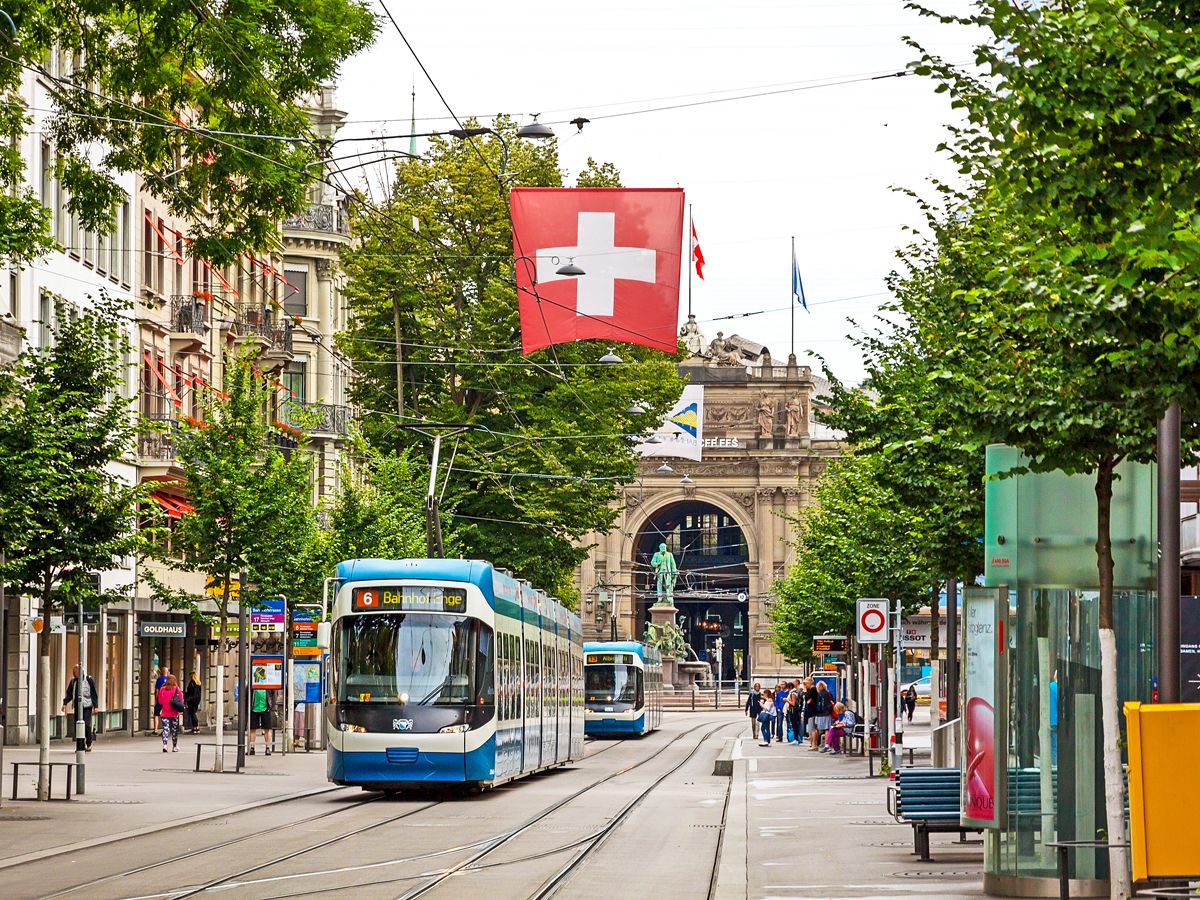 Trams on Zurich street with Swiss flag flying overhead