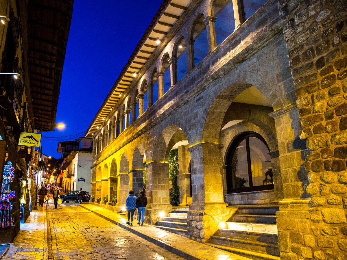 Two people walking beside Belmond El Monasterio in Cusco at night