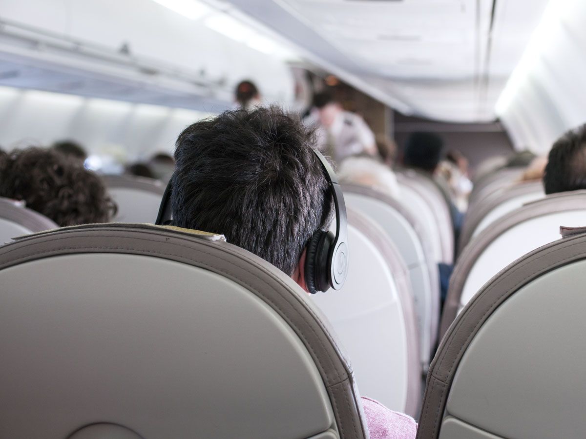 Passenger wearing headphones on airplane, seen from behind