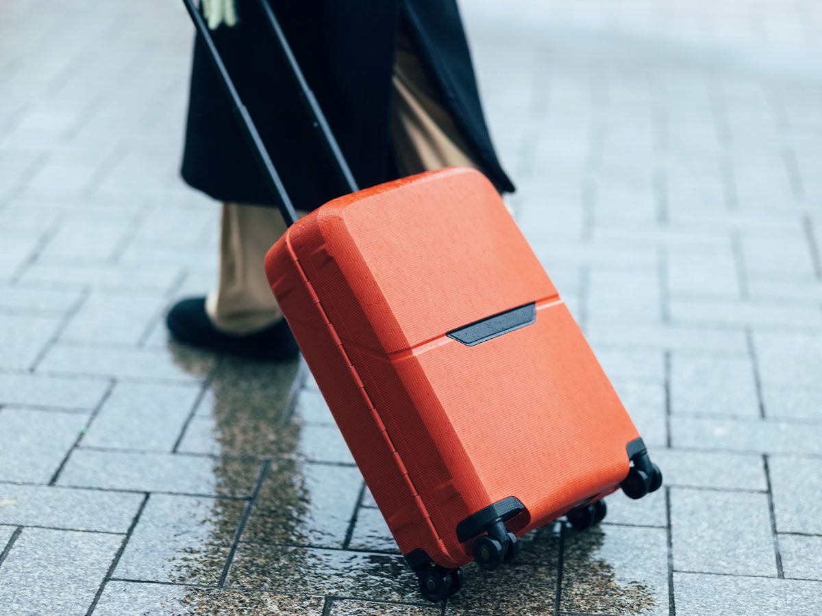 Person rolling suitcase on rainy sidewalk