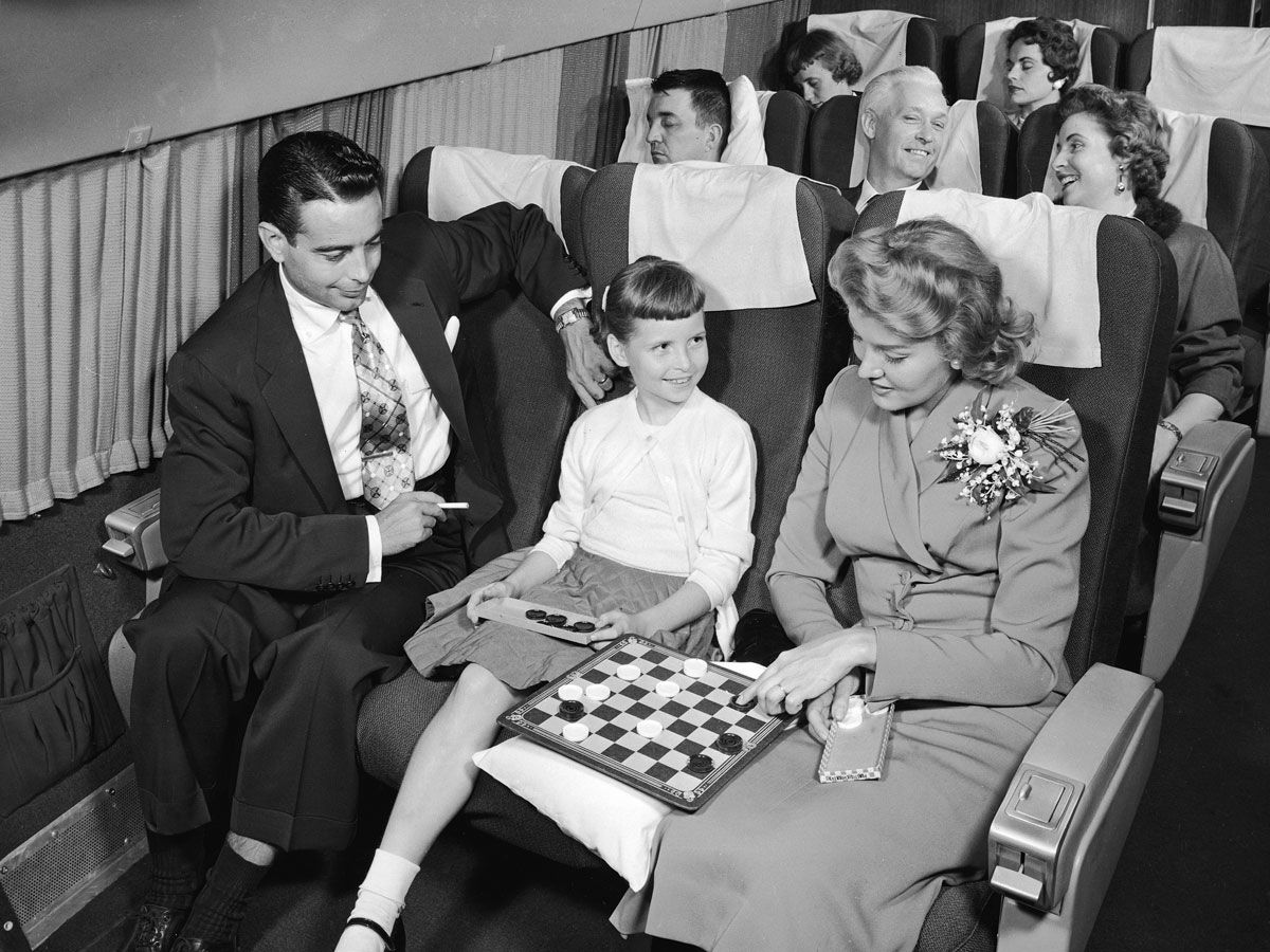 Historical photo of a father, daughter, and mother playing checkers on airplane