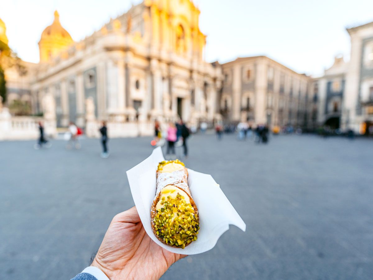 Person holding cannoli in square of Catania, Sicily 