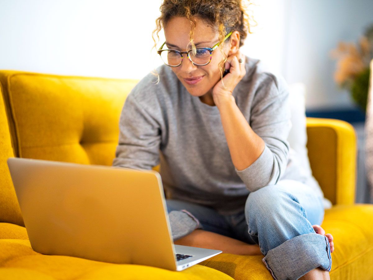Woman sitting on yellow couch using laptop computer