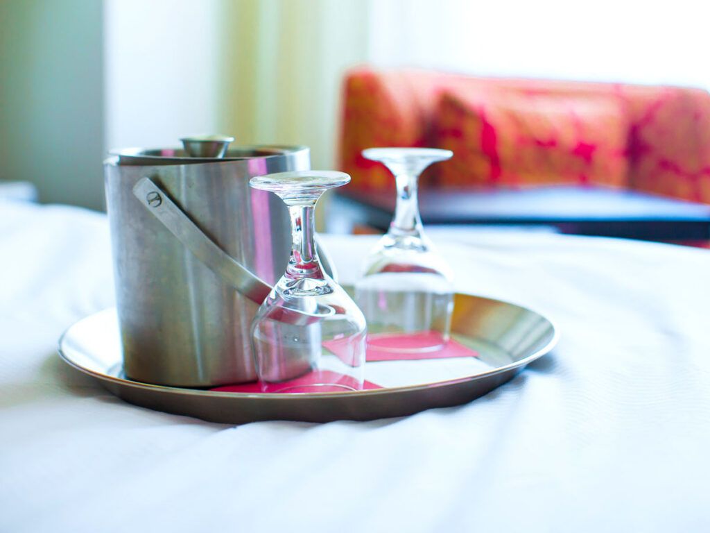 Tray with ice bucket and upside-down wine glasses on bed