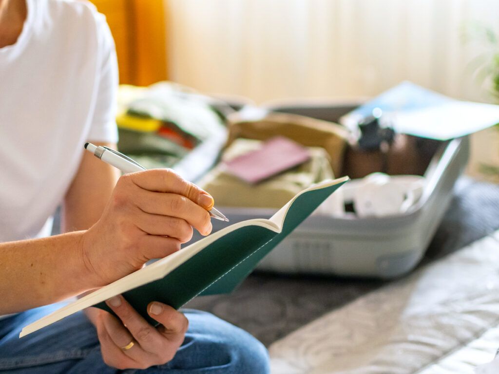 Person writing in notebook next to open suitcase